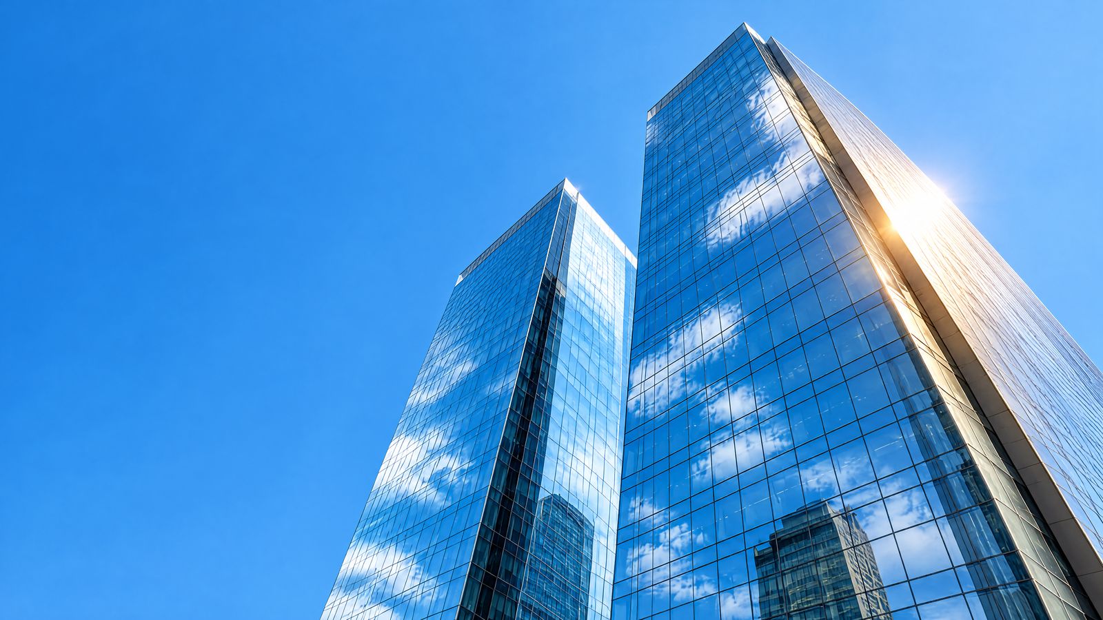 Dos torres corporativas de vidrio vistas desde la calle, reflejando el cielo azul